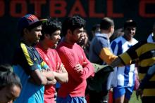 Three teenage rugby players standing on sideline watching.