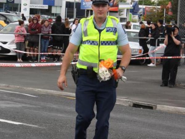 A Police officer takes flowers from the crowd to place at the scene