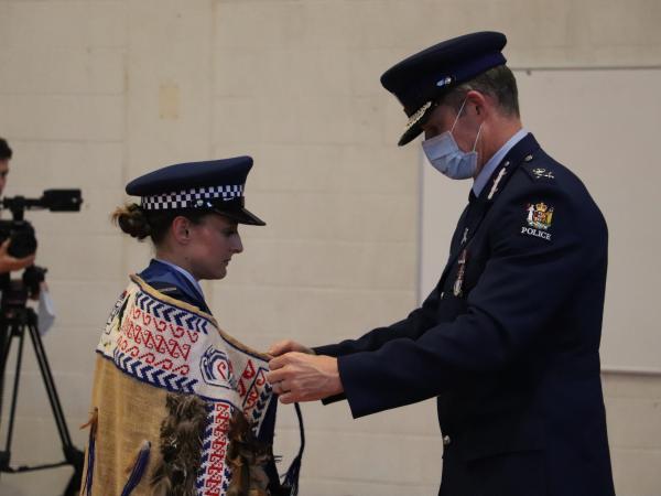 Commissioner Andrew Coster tying the Police College korowai around Lauren Recny's shoulders.